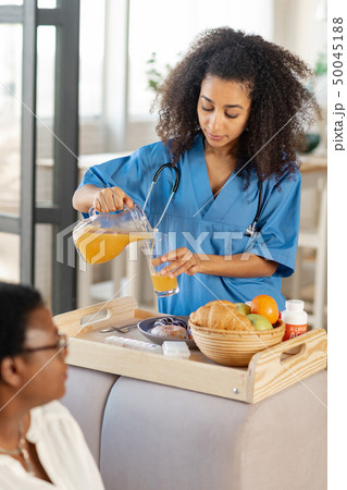 Curly dark-skinned nurse preparing breakfast for the patient 50045188