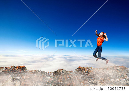 Redhead woman jumps over cliff on blue sky background. Redhead woman jumps over cliff on blue sky background. 50051733