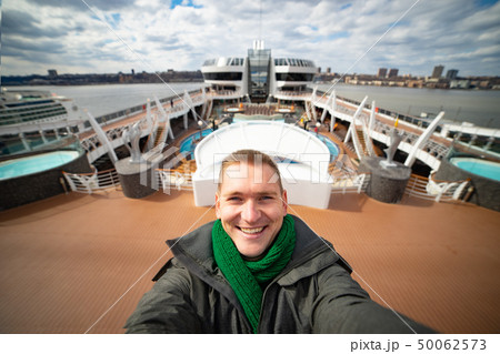 Young man makes selfie with huge cruise ship and city on background. Concept of happy vacation and Young man makes selfie with huge cruise ship and city on background. Concept of happy vacation and 50062573