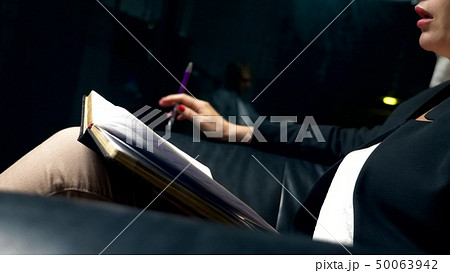 close-up. a woman talks to someone and takes notes in a notebook while sitting in the evening in a close-up. a woman talks to someone and takes notes in a notebook while sitting in the evening in a 50063942