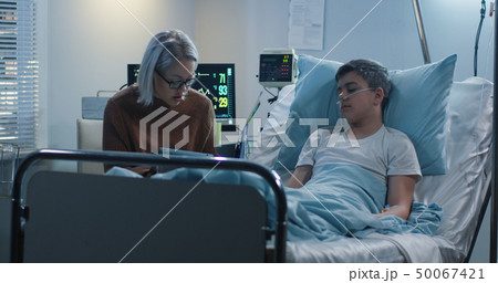 Mother reading aloud to sick son 50067421