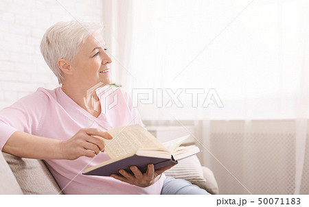 Dreamy senior woman relaxing at home with favorite book 50071183