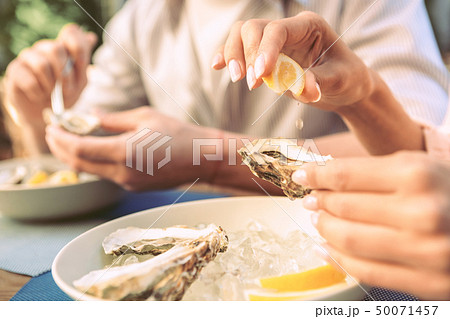 Girl with nude nails dripping lemon juice on opened oyster Girl with nude nails dripping lemon juice on opened oyster 50071457