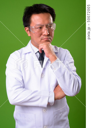 Mature Japanese man doctor wearing protective glasses against green background 50072005