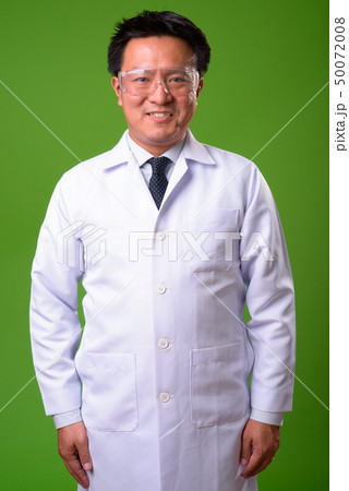 Mature Japanese man doctor wearing protective glasses against green background Mature Japanese man doctor wearing protective glasses against green background 50072008