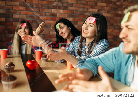 Smiling friends playing sticker notes to forehead Smiling friends playing sticker notes to forehead 50072322