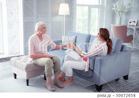 Loving grey-haired mother giving glass of water to her pregnant daughter Loving grey-haired mother giving glass of water to her pregnant daughter 50072658