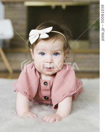 Baby girl wearing bow hair band lying on rug 50081036