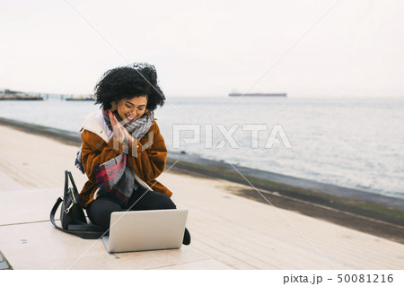 Young woman using laptop on waterfront in Lisbon, Portugal 50081216
