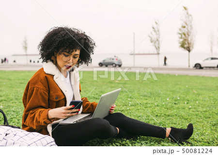 Young woman using laptop and smart phone in park 50081224