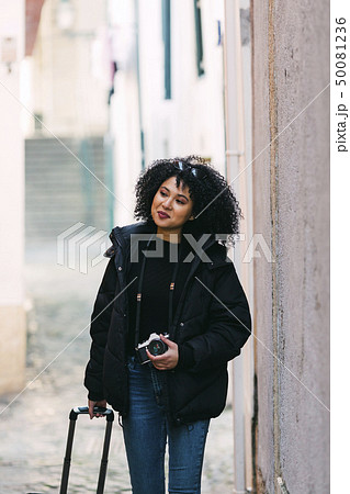 Young woman holding camera and suitcase in alley 50081236