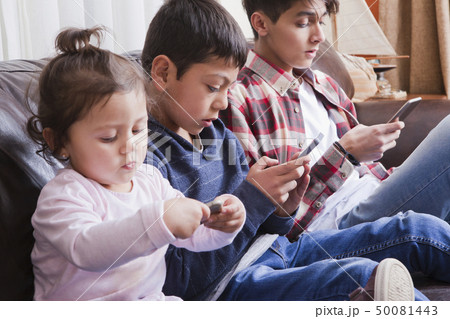 Siblings using smart phones on sofa 50081443