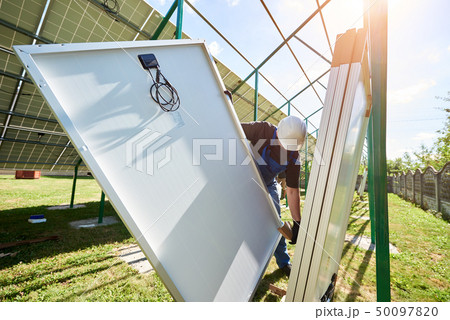 Professional worker wearing white protective helmet, mounting solar pannels on metal construction 50097820