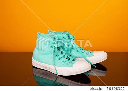 Turquoise sneakers on black glass table and yellow background. 50108392