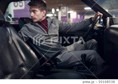 Photo from side of male driver looking back while sitting in car . 50108536