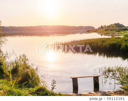 Empty bench near the river at sunset. Away from the hustle and bustle. Sun setting over the horizon 50112161