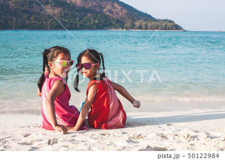 Two asian girls sitting and playing on the beach 50122984