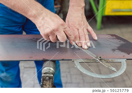 Metalworker with angle meter measuring strip of metal 50125779