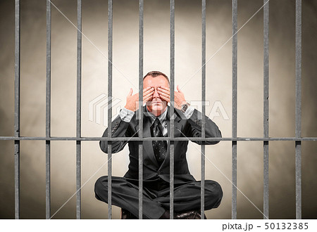 man sitting behind the bars of a prison 50132385