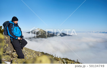 Hiker on rocky hill on background of valley with white clouds, snowy mountains and blue sky. 50134749