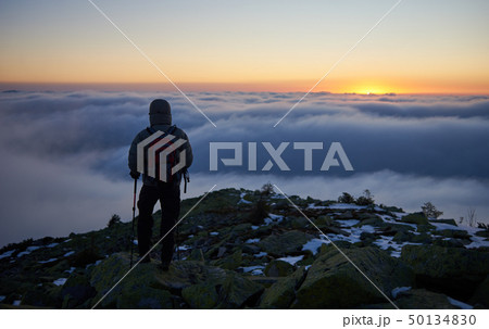 Tourist with backpack hiking on rocky mountain peak on background of foggy valley and blue sky at 50134830