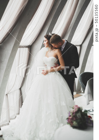 Lovely happy wedding couple, bride with long white dress posing in beautiful city Lovely happy wedding couple, bride with long white dress posing in beautiful city 50135560