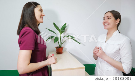 Friendly nurse on reception is talking with patient young woman, side view. 50138005