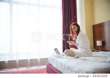 A ginger woman sitting on the bed in the hotel room A ginger woman sitting on the bed in the hotel room 50161839