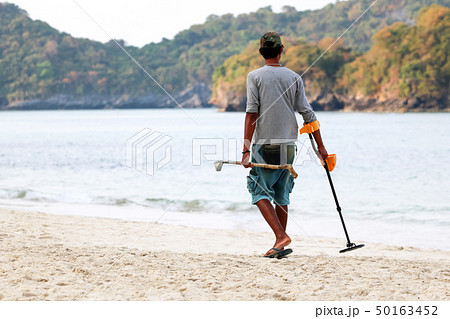 Asian male uses metal detector to find objects on 50163452
