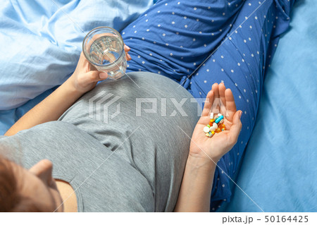 Pregnant woman with stomach and holding in her hands and pills and glass of water. Treatment of 50164425