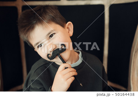 Happy kid posing with a fake moustache on black background Happy kid posing with a fake moustache on black background 50164438