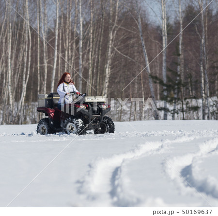 A winter forest. A woman with ginger hair riding big snowmobile A winter forest. A woman with ginger hair riding big snowmobile 50169637