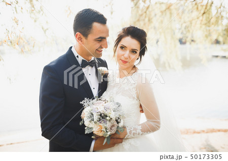 Romantic, fairytale, happy newlywed couple hugging and kissing in a park, trees in background Romantic, fairytale, happy newlywed couple hugging and kissing in a park, trees in background 50173305