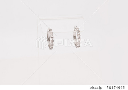 Pair of white golden diamond earrings on transparent stand. Golden earrings with diamonds, luxury 50174946