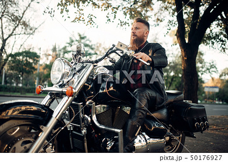 Biker sitting on a motorcycle leaning on a helmet 50176927
