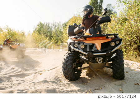 Two atv riders in helmets ride in a circle on sand Two atv riders in helmets ride in a circle on sand 50177124