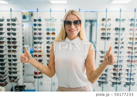 Female buyer tries on sunglasses in optics store Female buyer tries on sunglasses in optics store 50177233