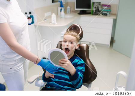 Little boy sitting in dantist chair with mirror. Male patient look at his teeth 50193357
