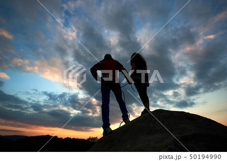 Young woman and man standing on the rock and watching for running clouds. With beautiful sunset on 50194990