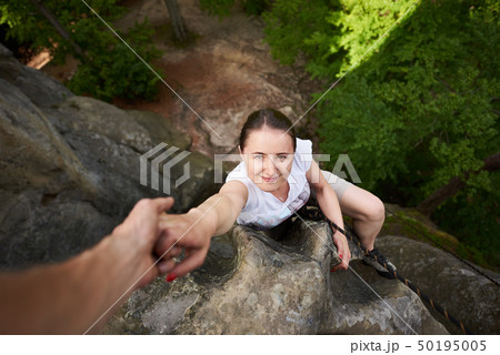 Beautiful young woman climbing on rock outdoors in summer. Top view. Happy girl climbing rock Beautiful young woman climbing on rock outdoors in summer. Top view. Happy girl climbing rock 50195005