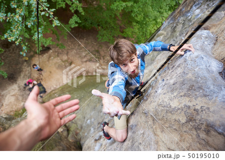 Climber rock climbing overhanging cliff with rope. Asking for help. Man helping his friend to climb 50195010