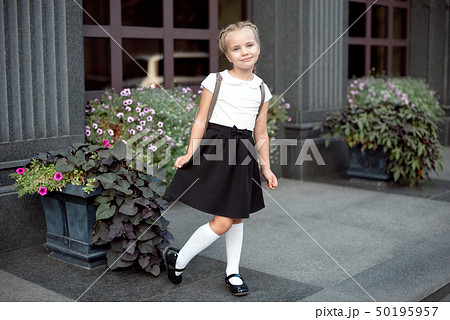 Full-length of a little smiling girl in school uniform posing against a school entrance background 50195957