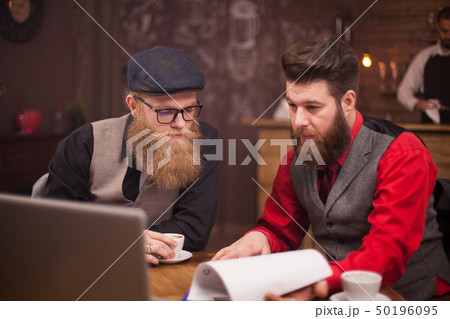 Two bearded collegues working together on a computer in a coffee shop 50196095