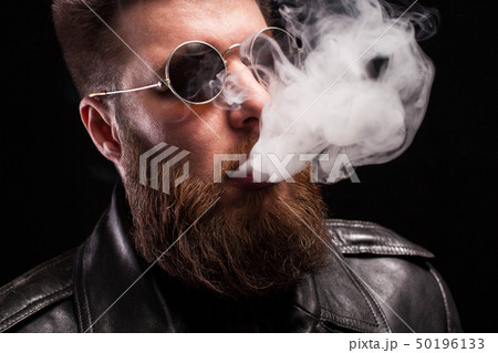 Close up portrait of confident bearded man wearing black leather jacket and sunglases smoking Close up portrait of confident bearded man wearing black leather jacket and sunglases smoking 50196133