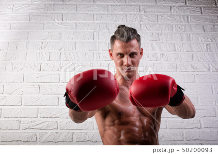 Portrait of handsome boxer man standing on the bric wall and looking at camera with intense gaze Portrait of handsome boxer man standing on the bric wall and looking at camera with intense gaze 50200093