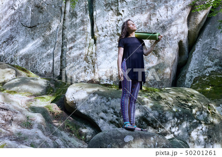 Young attractive girl in the mountains is holding a yoga mat Young attractive girl in the mountains is holding a yoga mat 50201261