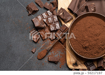 Dark Chocolate chunks and cocoa powder in wooden bowl on dark concrete background Dark Chocolate chunks and cocoa powder in wooden bowl on dark concrete background 50217197