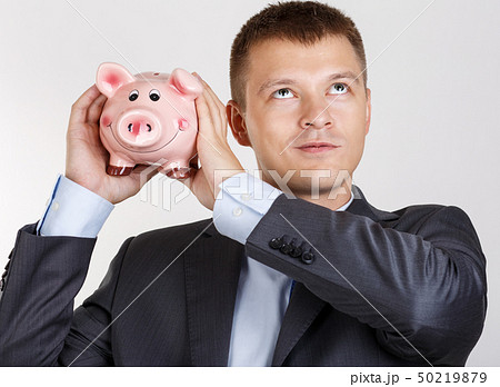 Businessman in suit and tie shaking funny piggybank Businessman in suit and tie shaking funny piggybank 50219879