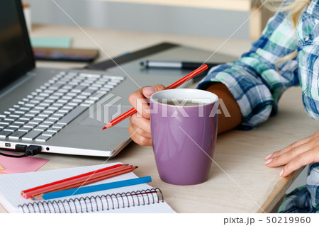 Female designer hands holding cup of hot beverage and drawing with pencil Female designer hands holding cup of hot beverage and drawing with pencil 50219960