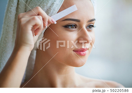 Beautician waxing young woman's eyebrows in spa center 50220586